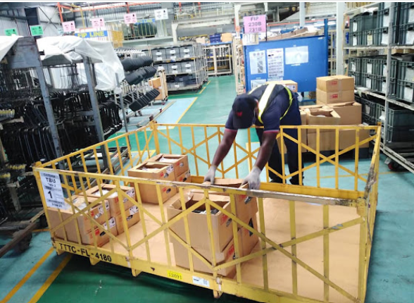 A worker handling cartons on a yellow materials trolley inside an industrial facility